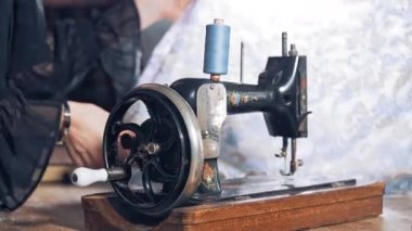 Atölyede çalışan bir kadın terzinin arka planında eski siyah dikiş makinesi. Profesyonel terzi, atölyede güzel malzemelerle çalışıyor..