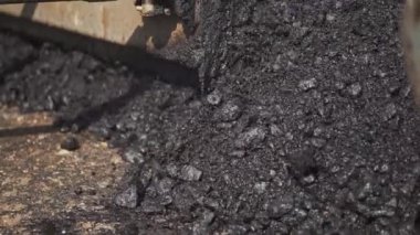 Kaldırım makinesinden yola dökülen sıcak asfalt yakın plan. Yol yapımı sırasında asfalt kaldırım taşı makinesi. Ağır kamyon siyah ziftlenir.