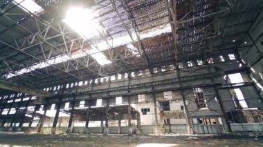 Çukur çatısı olan harap bir bitki ve içinde güneş parlıyor. Duvarlarında ve tavanında hasarlı delikler olan terk edilmiş bir binanın boş alanı. Kamera yukarı hareket ediyor.