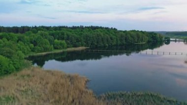 Yeşil ormanın yakınındaki güzel nehrin üzerindeki hava manzarası. Sık ormanlarla çevrili nehirde güneşli bir yaz günü. İnsansız hava aracı şehrin doğal arka planında ilerliyor..