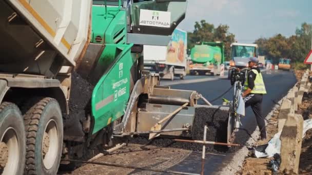 大的绿色摊铺机在路上喷出沥青和一个工人 夏天工作时使用的沥青喷雾器 道路工程期间带测量带的男工 — 图库视频影像