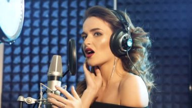 Ses kayıt stüdyosu. Kulaklıklı ve stüdyo mikrofonlu bir kadın şarkı söylüyor. Yavaş çekim