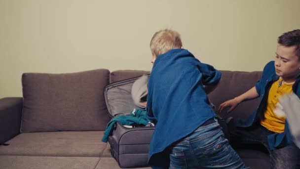 两个好奇的男孩正在把衣服放进行李箱 准备回家旅行 活跃的兄弟们在房间里一起把东西装进旅行袋里 慢动作 — 图库视频影像