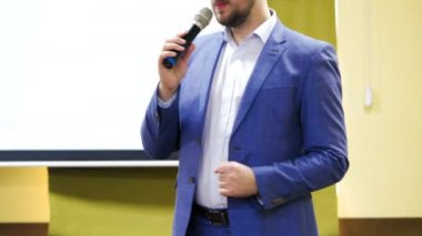 Mavi ceketli bir adam mikrofona doğru konuşuyor. Bir konferans salonunda seminere başkanlık eden erkek eğitmen..