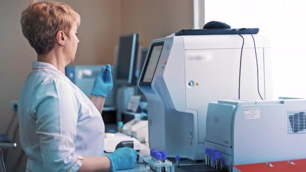 Wissenschaftlerin mixt im Labor ein Fläschchen mit Flüssigkeit in ihrer Hand. Technikerin arbeitet mit Reagenzgläsern, während sie in der Klinik vor der Kontrollmaschine steht.