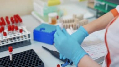 Profesyonel laboratuvar teknisyenlerinin elleri bir sürü sıvı şişesiyle çalışıyor. Steril masa, farklı raflarda test tüpleri ile tıbbi laboratuarda kan örneği..