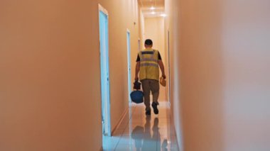 Koruyucu kıyafetli ve çantalı bir adamın koridordan geçişi. Erkek işçi laboratuardan test tüpleriyle özel bir çanta hazırlıyor..