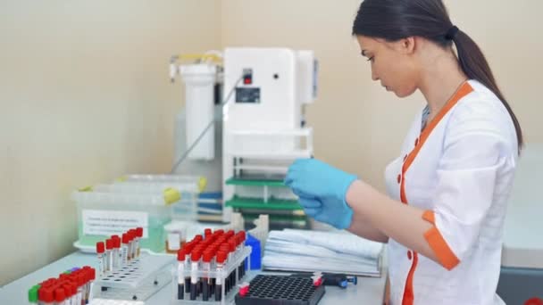 穿着医疗制服的漂亮的实验室技术人员用血样工作 女性研究人员正在实验室里与许多瓶液体一起工作 — 图库视频影像