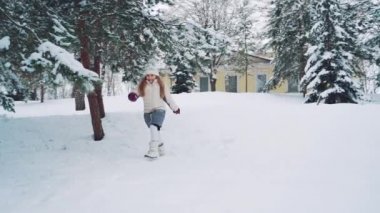 Kışın güzel köknar ağaçlarının arasında karda koşan tatlı küçük kız. Bir kız arkadaşının beyaz kardan dışarı çıkmasına yardım edecek. Yavaş çekim.