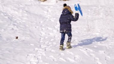 Çocuklar doğada karlı kış yürüyüşlerinde eğleniyor, oynuyor ve gülüyor. Buz mevsimi. Plastik kızaklı şirin çocuklar kış günü açık havada bir tepeye çıkıyorlar. Kış oyunları ve eğlence