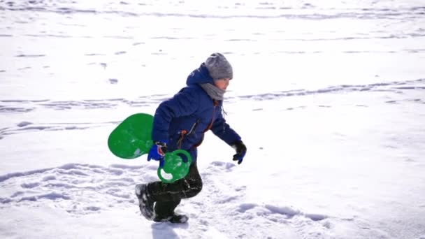 孩子们玩得很开心 在大自然里 在雪地的冬天散步 冬天结霜了 可爱的小男孩拿着塑料雪橇爬上了一座小山 — 图库视频影像