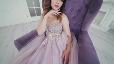 Mor koltukta oturan seksi elbiseli çekici kız. Güzeller güzeli gelin güzel bir iç odada poz veriyor. Gelinlik içinde güzel bir manken. Kamera yukarı hareket ediyor.