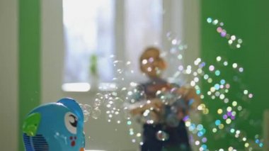 Küçük mutlu çocuk odada sabun köpüğü patlatıyor. Meraklı çocuk evde yuvarlak kabarcıklar yakalıyor. Balık şeklinde baloncuk üfleyici ve yanında küçük bir çocuk oynuyor..