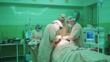 Profesyonel cerrahların takım çalışması ameliyathanede. Özel üniformalı doktorlar klinikteki yeşil arka plandaki bir hastanın ameliyat sırasında tıbbi ekipmanlarla çalışırlar..