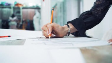 Profesyonel bir terzinin elleri masaya sivri bir kalemle çizim yapıyor. Terzi, işyerindeki bir kağıt parçasında elbisenin yaratıcı bir tasarımını yapıyor..