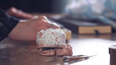 Tahta masadaki terzi için beyaz dantel bir süngerde iğne dikiyorum. Atölyede çalışan terzinin arka planında masanın üzerinde güzel bir iğnelik var. Yakın plan..