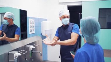 Doktor ameliyattan sonra bir kadınla sohbet ediyor ve ellerini yıkıyor. Klinikteki tuvalette iki doktor konuşuyor. Cerrah ellerini sabun ve suyla temizliyor..