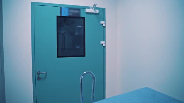 負傷した患者を運ぶための手術室と医療カートの青いドア 室内に光の廊下と新しいガーニーを空にします バックモーションカメラ — ストック動画