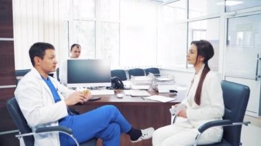 Profesyonel doktorlar modern kabinede oturup gevezelik ediyorlar. Sağlık görevlileri, bir erkek ve bir kadın sağlık kliniğinde siyah koltuklarda otururken sohbet ediyorlar..