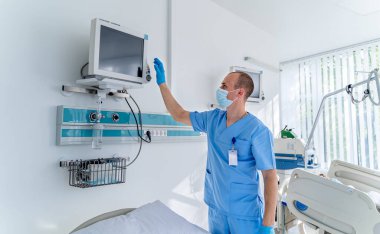 Mavi elbiseli ve maskeli doktor üzerinde sağlık parametreleri olan ekrana bakıyor. Tıbbi oda. İlk yardım. Canlandırma.
