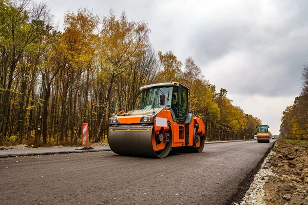 Road repair, compactor lays asphalt. Heavy special machines. Asphalt paver in operation. Side view. Closeup.