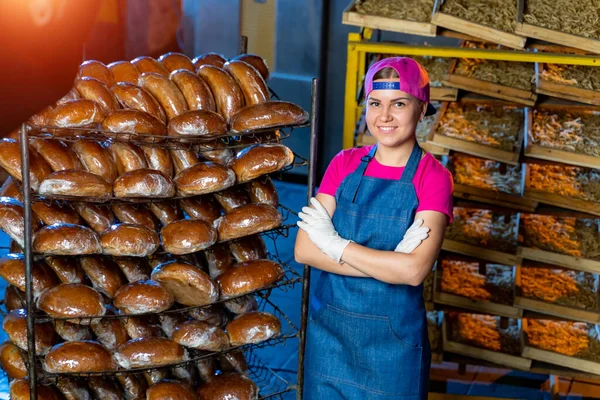 Portrait of a baker girl against the background of shelves with fresh bread in a bakery. Industrial bread production