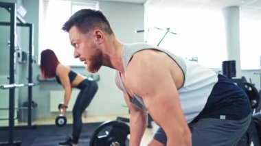 Kaslı bir adam ve spor salonunda ağırlık kaldıran genç bir kadın. Spor kulübünde spor yapan spor çifti. Atletik çift egzersizi birlikte bitirir ve halterleri yere koyar..