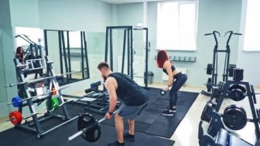 Modern spor salonunda koltuk değneklerini kaldıran atletik erkek ve kadının arka görünüşü. Güçlü çift, spor salonunda büyük bir aynanın önünde ağır ekipmanlarla fiziksel egzersiz yapıyor..