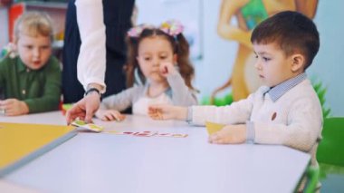 Çocuklar öğretmenleriyle birlikte sınıfta yuvarlak masada. İlkokulda resimlerle oynarken İngilizce okuyan küçük çocuklar..