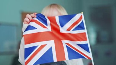 Sınıfta meyvelerin yerleşimiyle masada İngilizce öğrenen çocuklar. İngiliz bayrağını tutan ve eğitim merkezinin arka planında sallayan küçük kız..