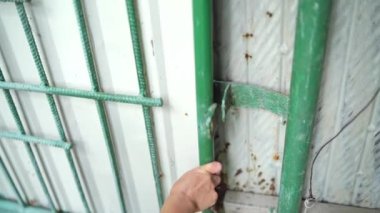 Kadının elleri anahtarı çelik bir kilitte döndürür ve eski metal kapıyı açar. Kadın anahtarı asma kilide sokuyor ve dışarıdaki kapıların kilidini açıyor. Yakın plan..