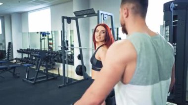 Spor elbiseli sağlıklı bir çift spor salonunda dambıl kaldırıyor. Çekici bir kadın ve yakışıklı bir erkek spor kulübünde dambıllarla spor yapıyor..