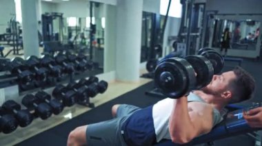 Spor elbiseli sağlıklı bir çift spor salonunda dambıl kaldırıyor. Çekici bir kadın ve yakışıklı bir erkek spor kulübünde dambıllarla spor yapıyor..