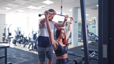 Genç atletik kadın spor salonunda otururken çıtayı kendine çekiyor. Özel antrenörüyle egzersiz yapan güzel bir kız. Spor ve sağlıklı yaşam tarzı.