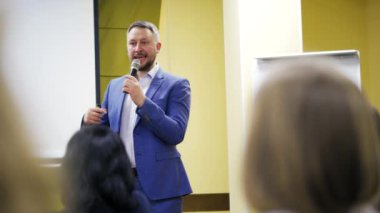 Deneyimli bir hoparlör mikrofona konuşuyor. Şık takım elbiseli yönetici, konferans salonunda seyircilere bir konuşma yapıyor..