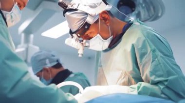 Tıbbi üniforma uzmanları hastanede bir operasyon yapıyorlar. Kafasında büyüteç olan cerrah ameliyathanede asistanlarla çalışıyor. Doktorun konsepti.