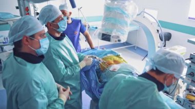 Bir grup cerrah monitöre bakarken ameliyat yapıyor. Koruyucu giysiler giyen uzmanlar tarafından işletiliyor. Klinikteki ameliyat sırasında modern teknolojiler.