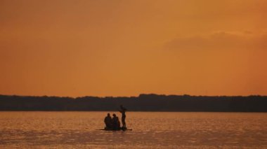 Mutlu adamlar turuncu gün batımında Katamaran 'da iyi vakit geçirirler. Katamaran 'da akşamları su üzerinde rafting yapan üç genç adam..