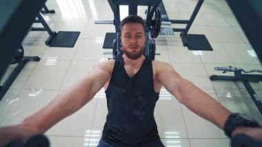Spor salonundaki atletik bir adamın yakın plan fotoğrafı. Adam siyah bir tişört giyiyor ve sırt ve kol kasları için modern bir simülatör üzerinde çalışıyor. Spor yaşam tarzı..