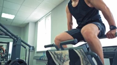 Modern bir simülatörde oturan güçlü bir antrenör ve bir kadın onu bacaklarından kaldırıyor. Bayan sporcu spor kulübünde spor antrenman makinesinde bacak egzersizi yapıyor..