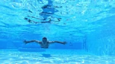 Tatil konsepti. Yüzme havuzunda yüzen mutlu genç adam. Adam suyun altına dalıyor ve kameraya doğru ilerliyor..