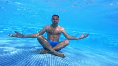 Adam yüzme havuzunun dibinde oturuyor. Sağlıklı bir adam yoga pozisyonunda mavi arka planda suyun altında oturuyor. Su altı sporu.