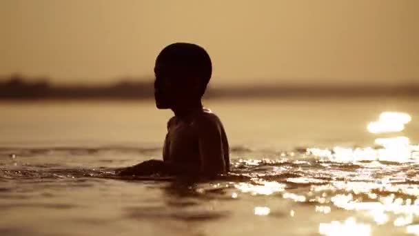 少年は日没時に川で泳ぐ アクティブな子供は夕方に水中でダイビングします 屋外で母親に泳いでいる子供のシルエット — ストック動画