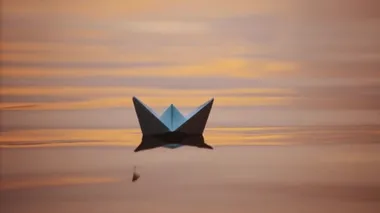 Origami teknesi akşam su yüzeyinde. Beyaz kağıttan tekne gölgesi suda yüzer. Yakın plan..
