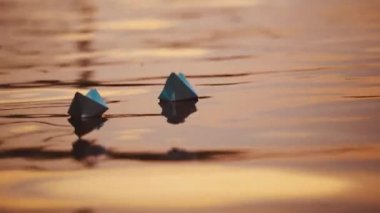 Açık denizde iki mavi kağıt gemi. Origami tekneleri akşamları su yüzeyinde yüzerler. Yakın plan..