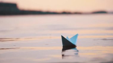 Akşam su yüzeyinde güzel bir kağıt tekne. Mavi bir origami gemisi, yansıması dışarıda sakince nehirde yüzüyor..