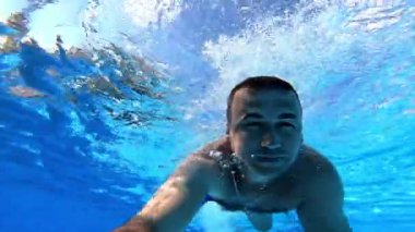 Yüzücü su altındaki kameraya bakarken ileri doğru yüzer. Yüzme havuzunda su altı kamerasıyla yüzen bir adam. Yaz tatili.