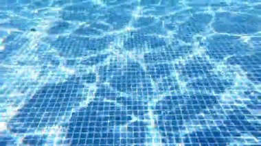 Yüzme havuzunun dibinde. Suyun altındaki güneş ışınlarının yansıması olan temiz su arka planı. Biri havuzda yüzüyor. Su altı kamerasından inanılmaz bir görüntü..