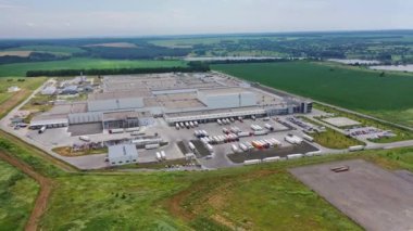 Büyük bir endüstriyel kompleksin hava görüntüleri. Birçok beyaz kamyon ve farklı arabalar büyük üretim fabrikasının yanındaki park yerindeler. Hava görünümü.