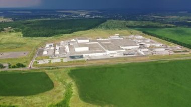 Üretim tesisine uzaktan hava görüntüsü. Yazın yeşil tarlalar ve ormanlarla çevrili büyük sanayi bölgesi. Kamera aşağı hareket ediyor.
